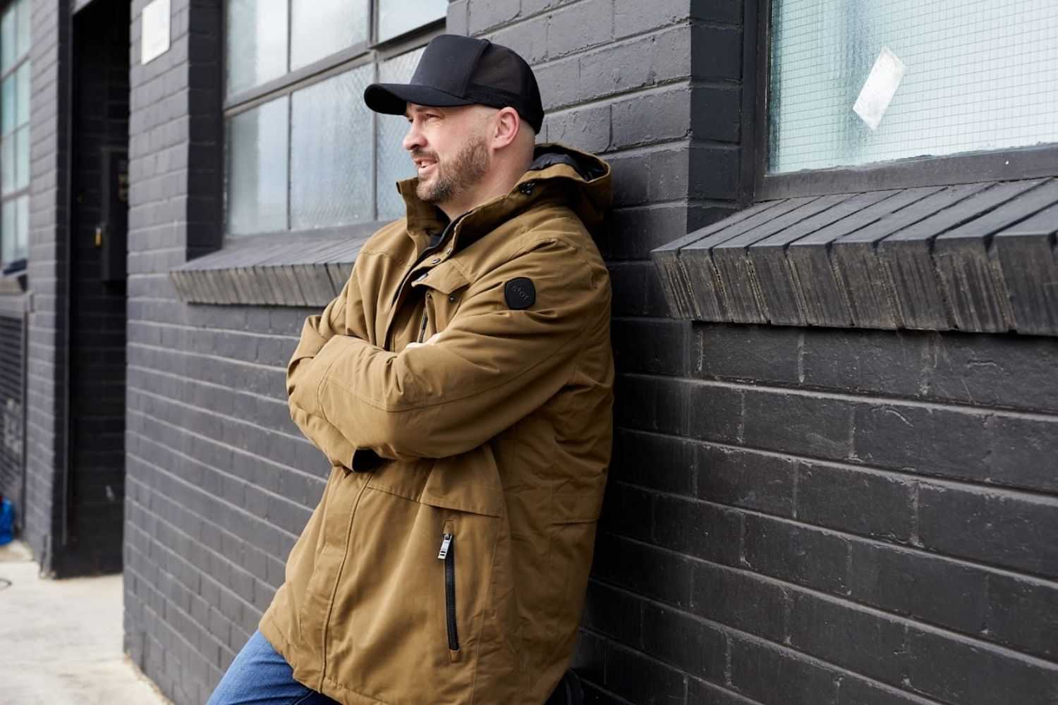 Man wearing brown winter jacket standing outdoors in urban setting.