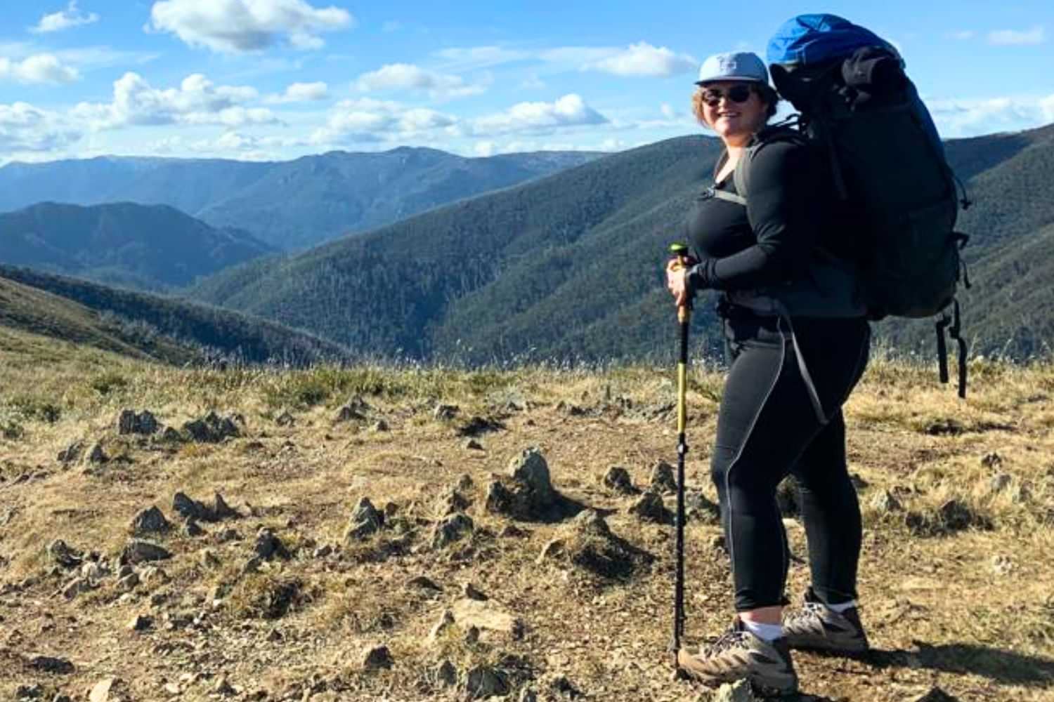 Plus size woman hiking mountain trail with backpack and trekking poles.