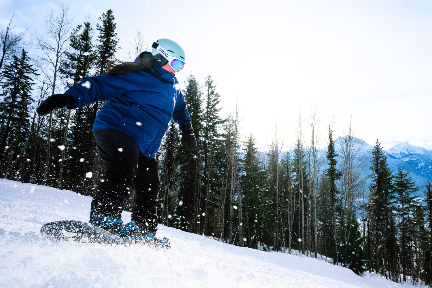 female plus-size snowboarder wearing a blue jacket and black pants snowboarding down the mountain while catching a little air