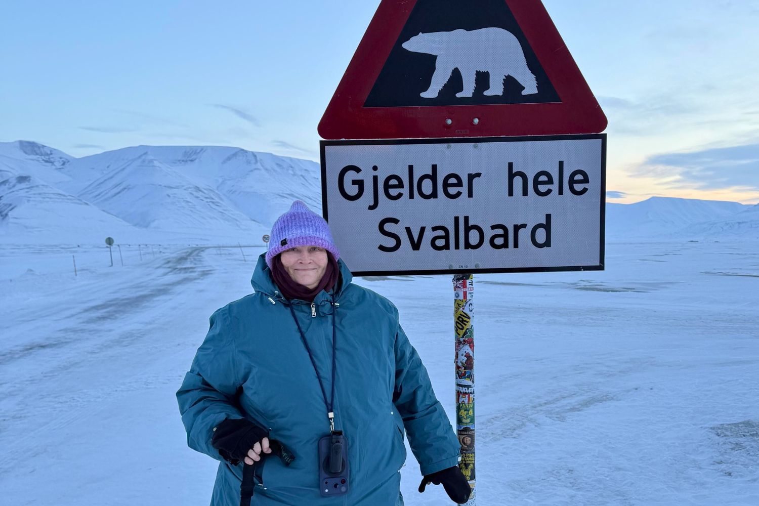 Plus-size woman wearing a warm winter jacket and banie in Norway standing next to a Svalbard sign with a polar bear