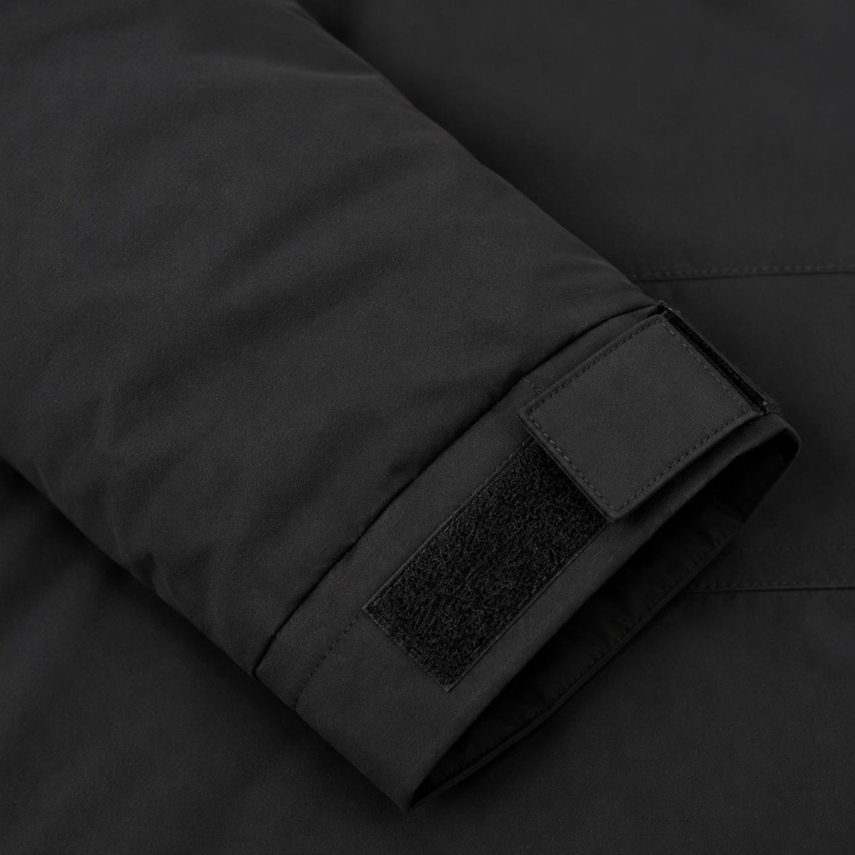 Close-up of a black jacket sleeve cuff with a hook-and-loop strap closure, shown against matching black fabric.