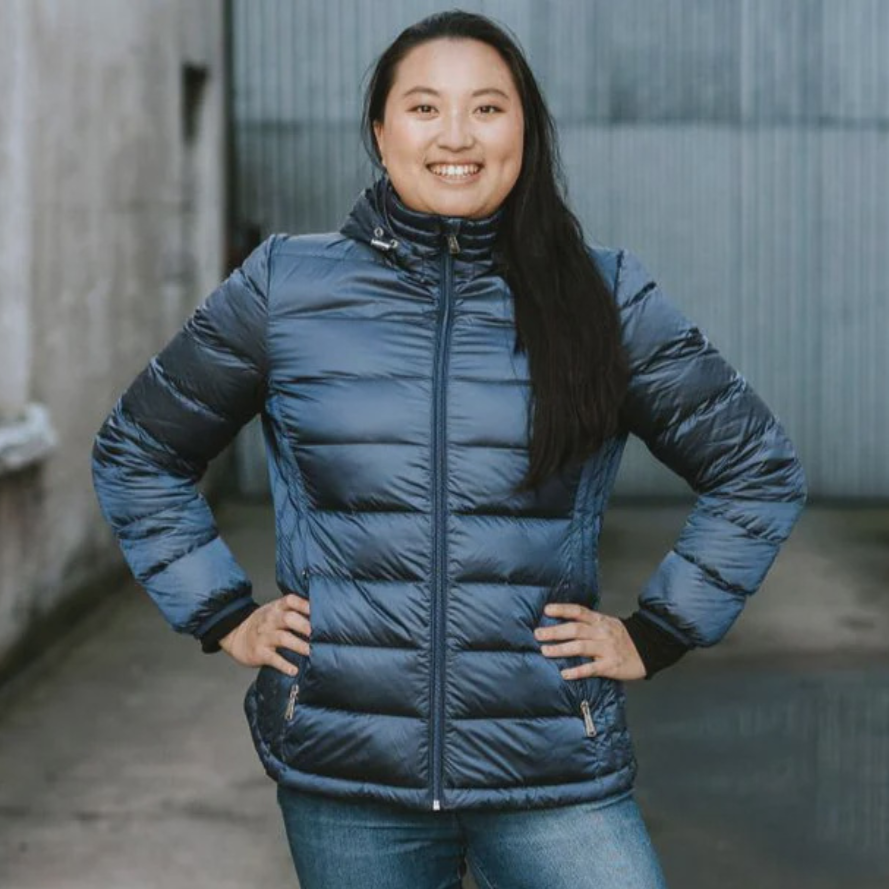 Person wearing a Moke down navy plus-size blue puffer jacket and jeans standing in an alleyway.