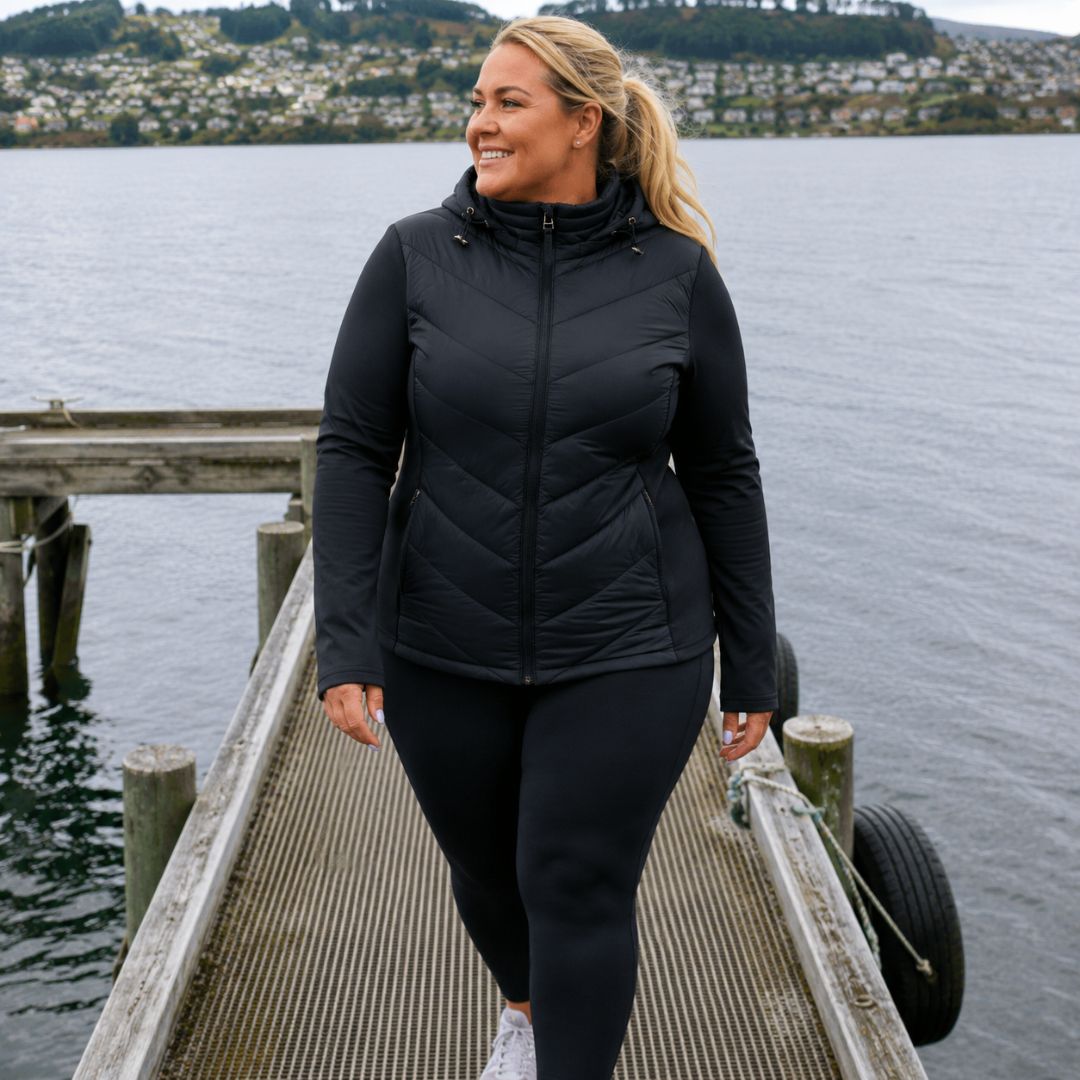 Front view of a smiling woman looking to the side while walking on a dock, wearing the zipped black Olive Packable Down Jacket.