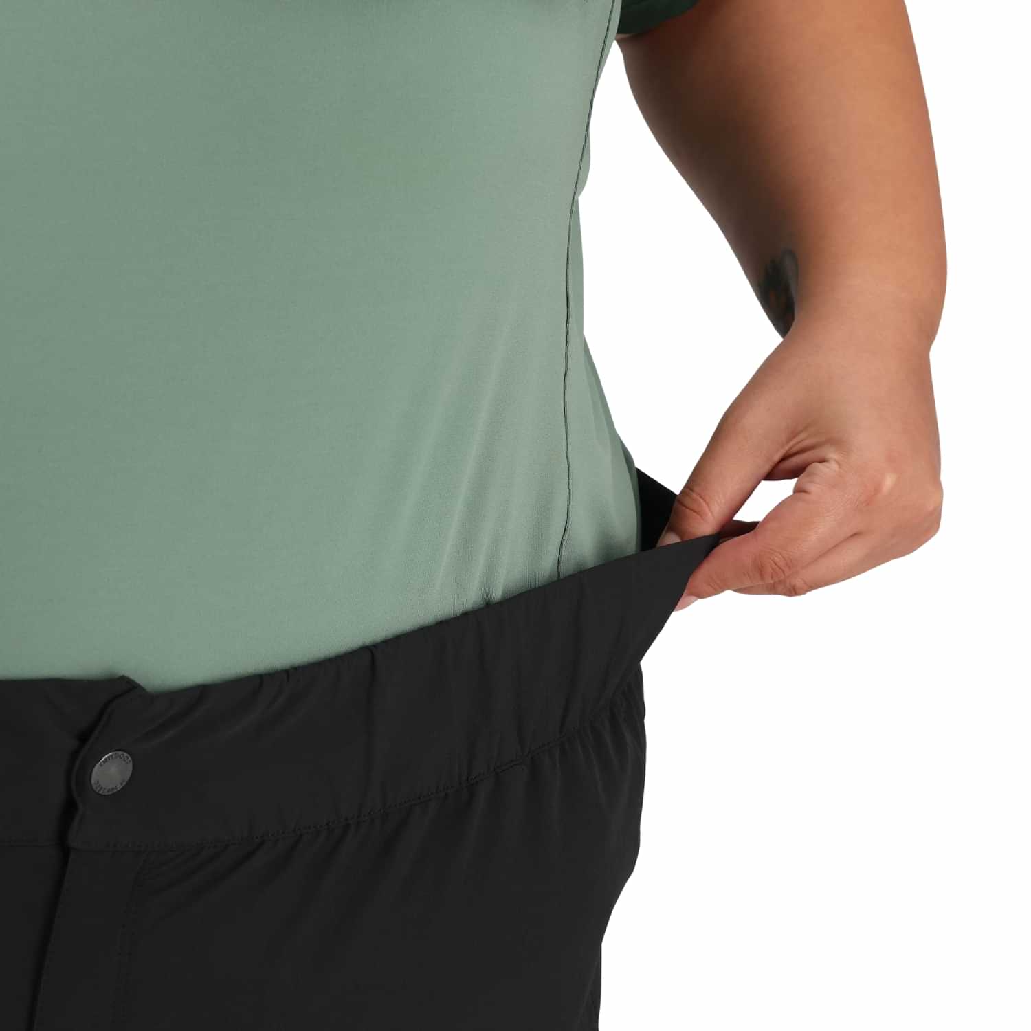 Person adjusting black pants with a green top on a white background