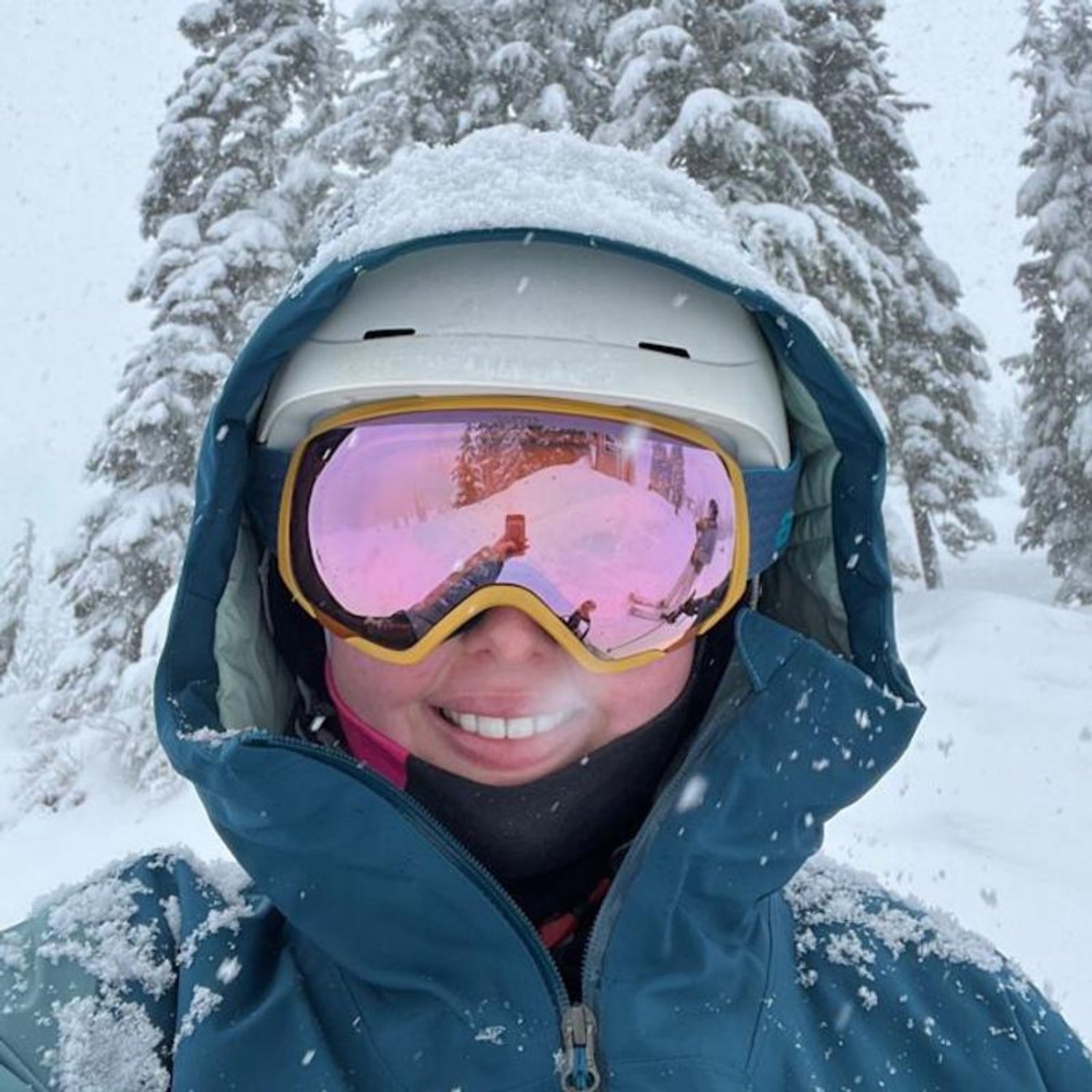 Person wearing ski goggles and helmet in a snowy landscape with trees.