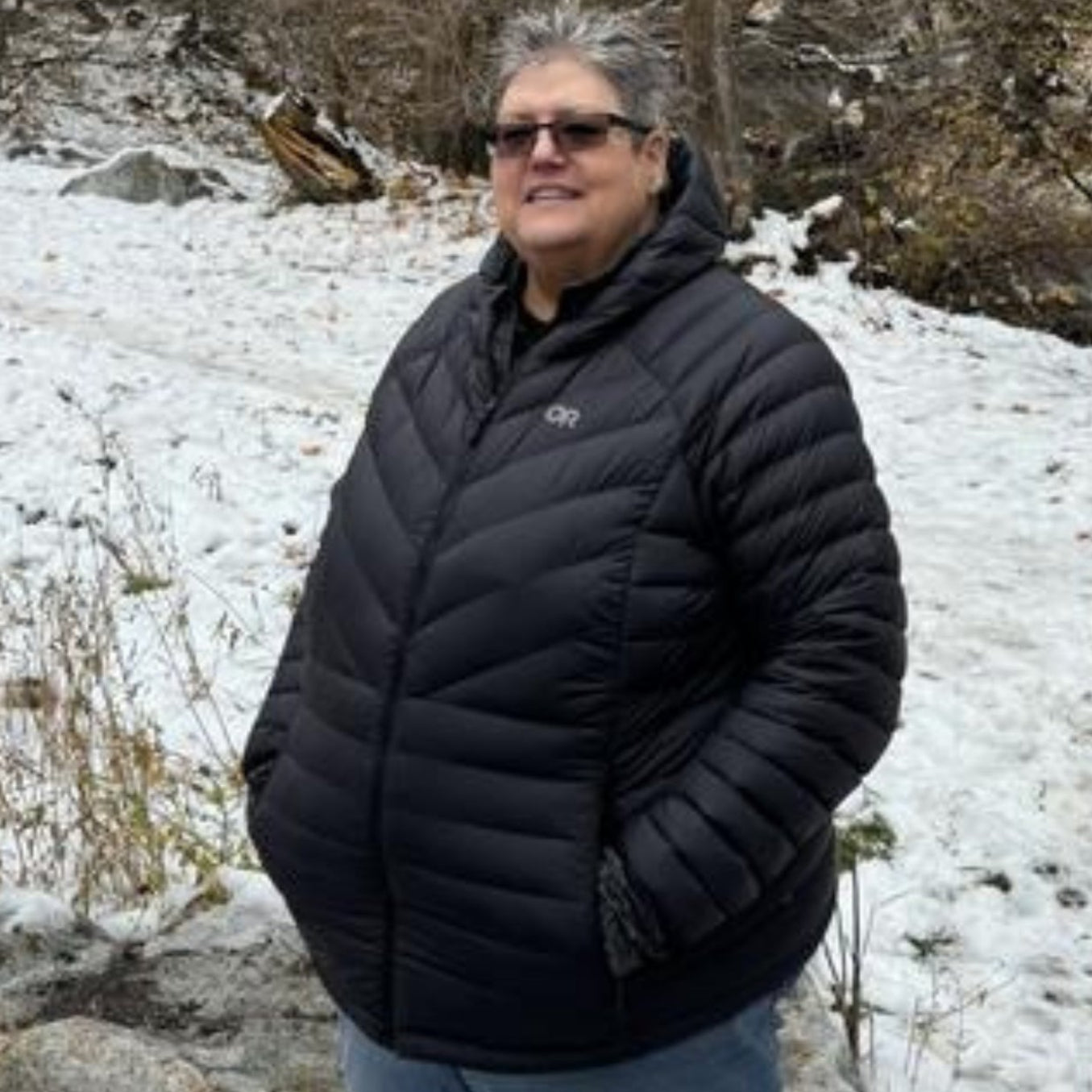 Plus size woman wearing an Outdoor Research black down puffer jacket standing in a snowy landscape