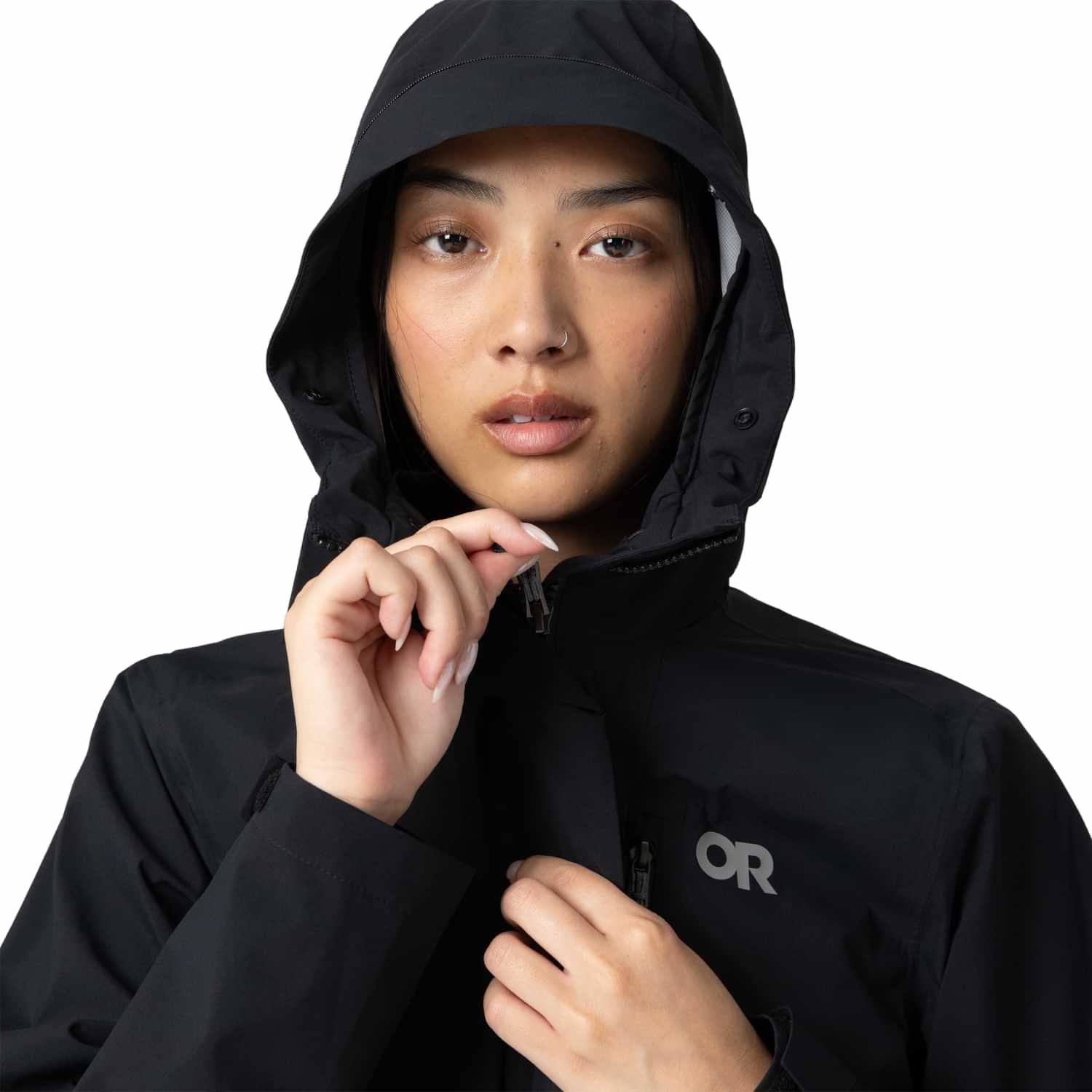 Close-up of a woman pulling up the front zipper of a black Outdoor Research Women's Plus Size Stratoburst Rain Jacket with the hood up.