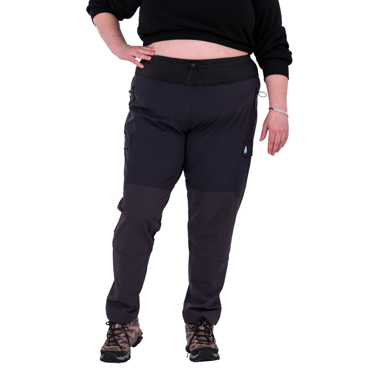 A pair of gray Thicket Adventure Brecken Women's Plus Size Hiking Pants with an adjustable waistband, displayed on a model wearing black top and standing against a white background.