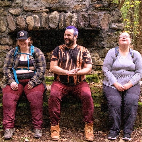 Three plus-size people sitting together in front of a stone wall in a forest setting