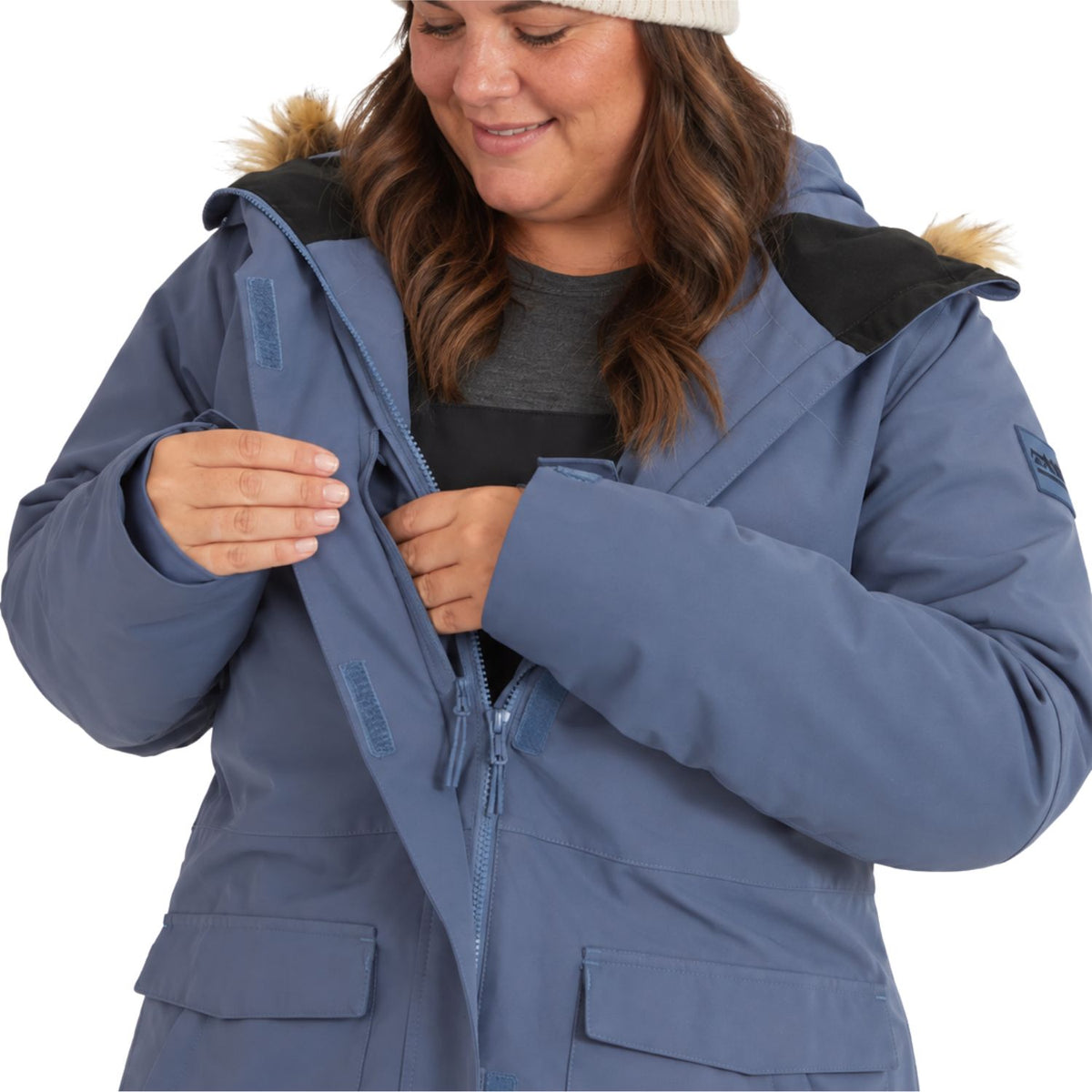 A woman wearing a slate blue hooded parka jacket with black shoulder panels and faux-fur trim, shown from the chest up against a plain white background.