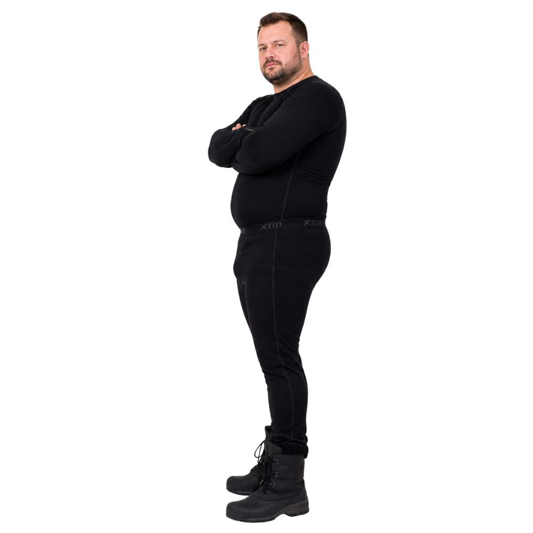 Profile view of a man with arms crossed modeling the black XTM Siberia Merino Wool Unisex Plus Size Thermal Pants and winter boots.