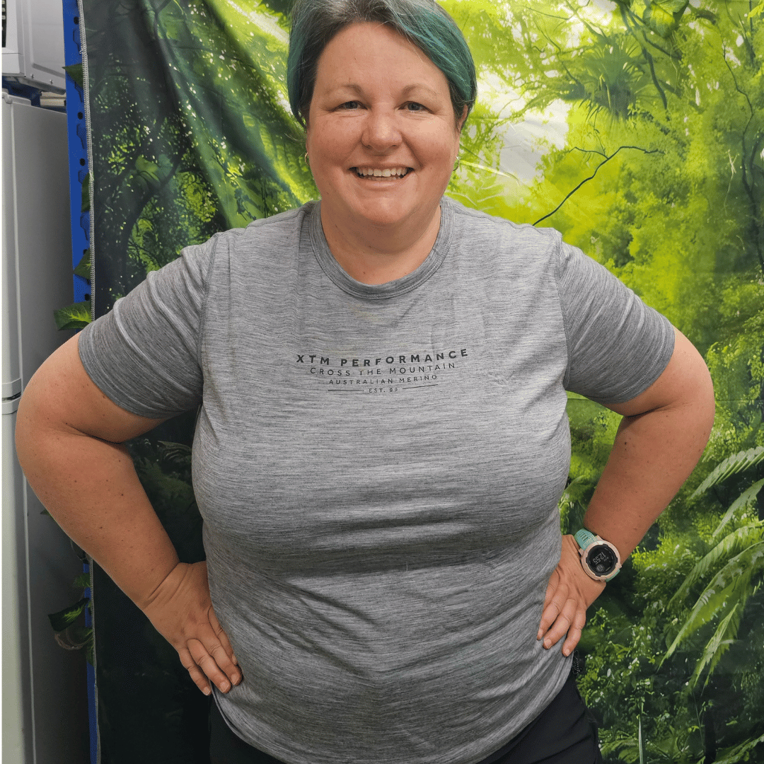 Person wearing a gray 'XTM Performance' t-shirt standing in front of a green forest background