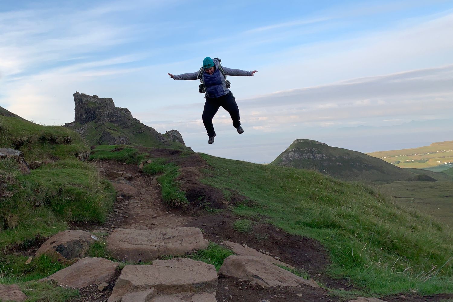 plus size woman wearing a backpack is jumping high on a mountain trail