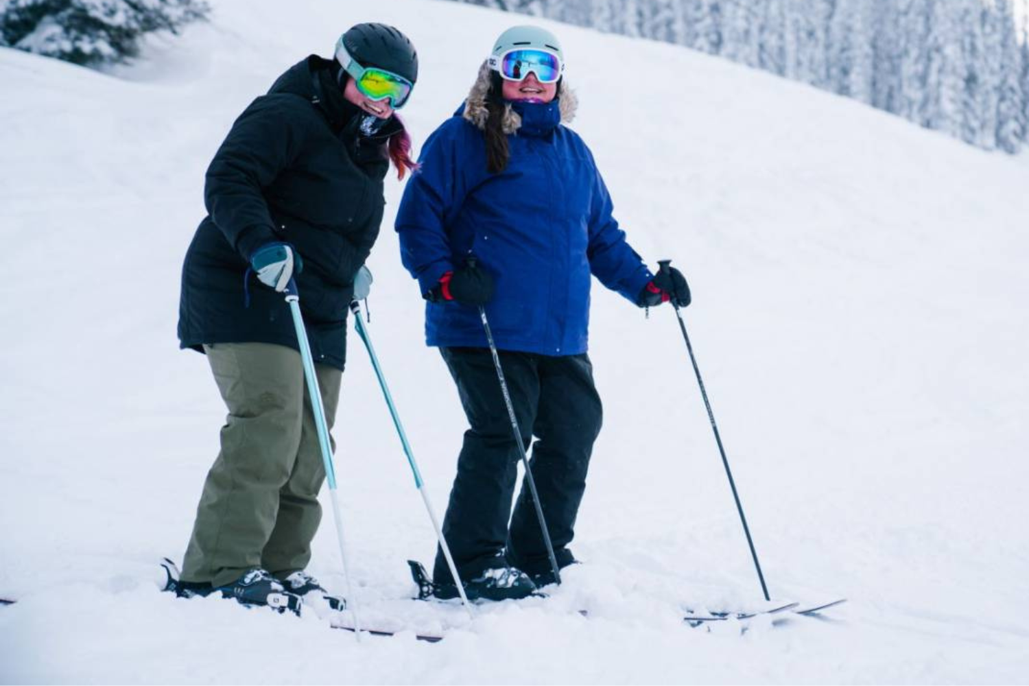 Two plus size women on skis on the side of ski run smiling and laughing together 