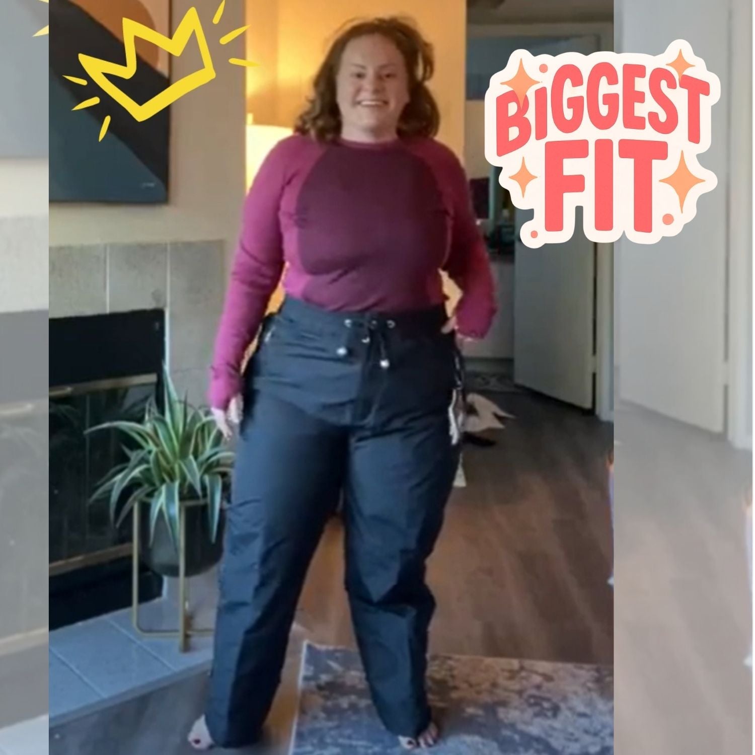 Smiling woman modeling the Aggress Plus Size Queen Snow Pants in black with a purple long-sleeve thermal top indoors.