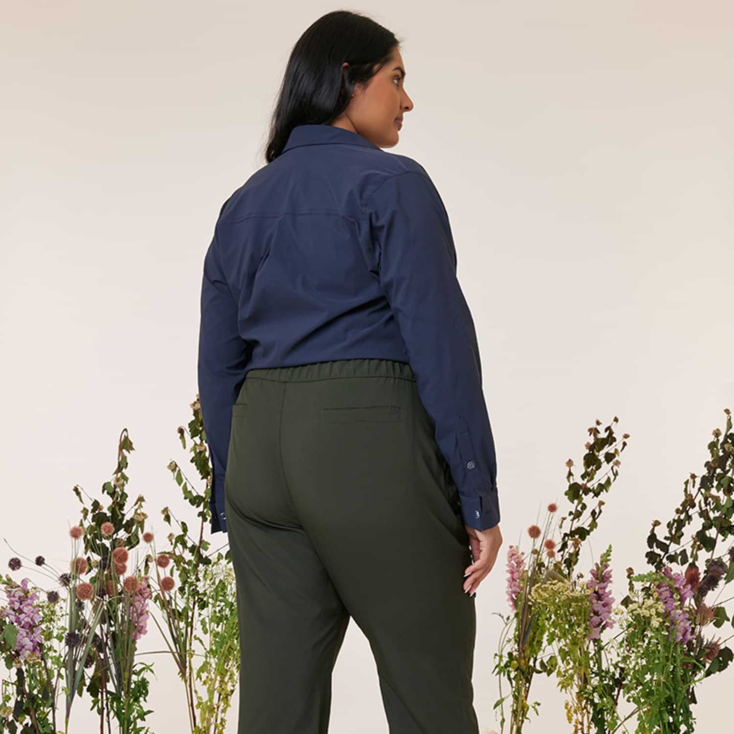 Rear profile view of a woman modeling the Amble Stirling Women's Plus Size Shirt in midnight dark blue with olive green pants.