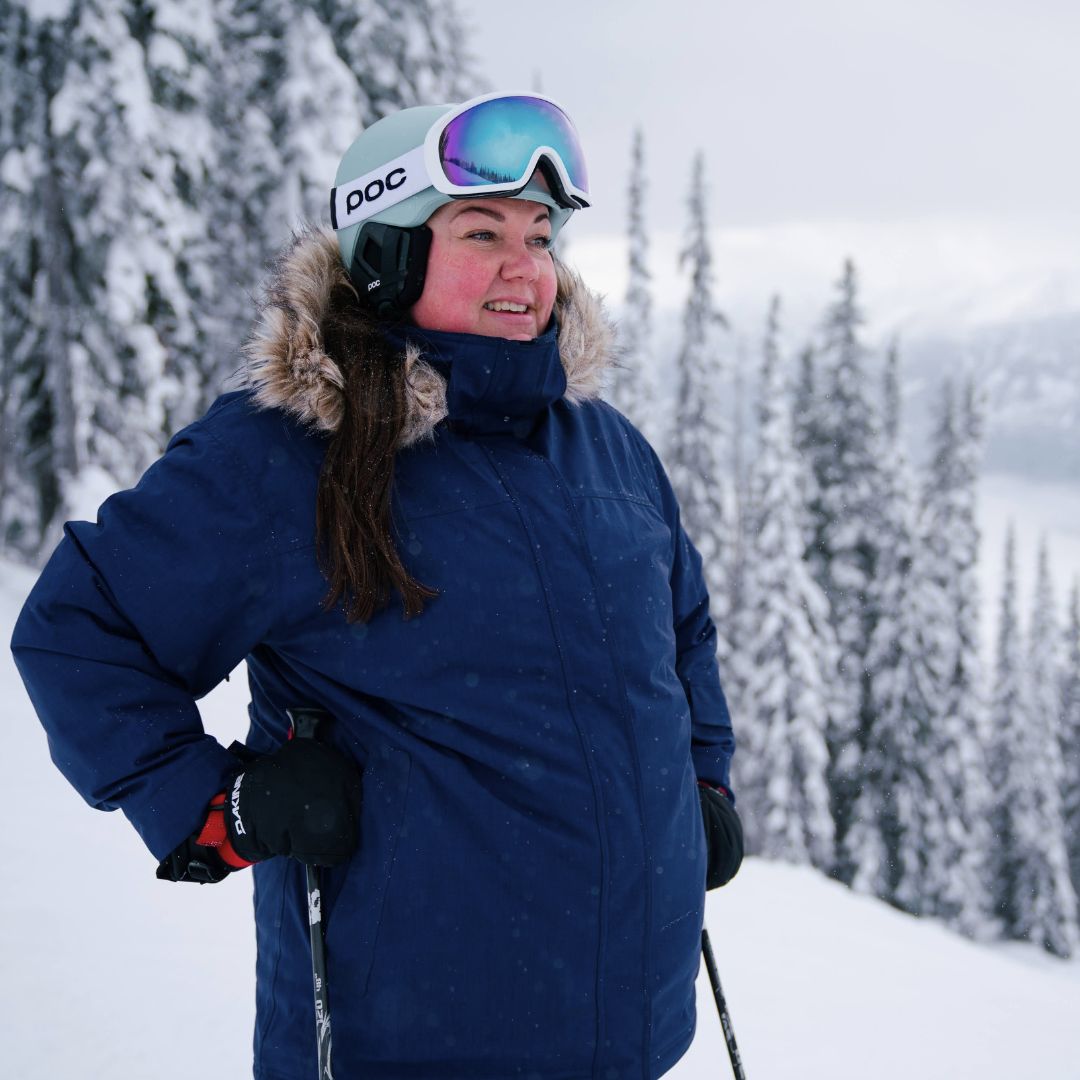 Woman skiing on a snowy mountain wearing the Cartel Brooklyn Stretch Women's Plus Size Ski Jacket in blue, a POC helmet, and goggles.
