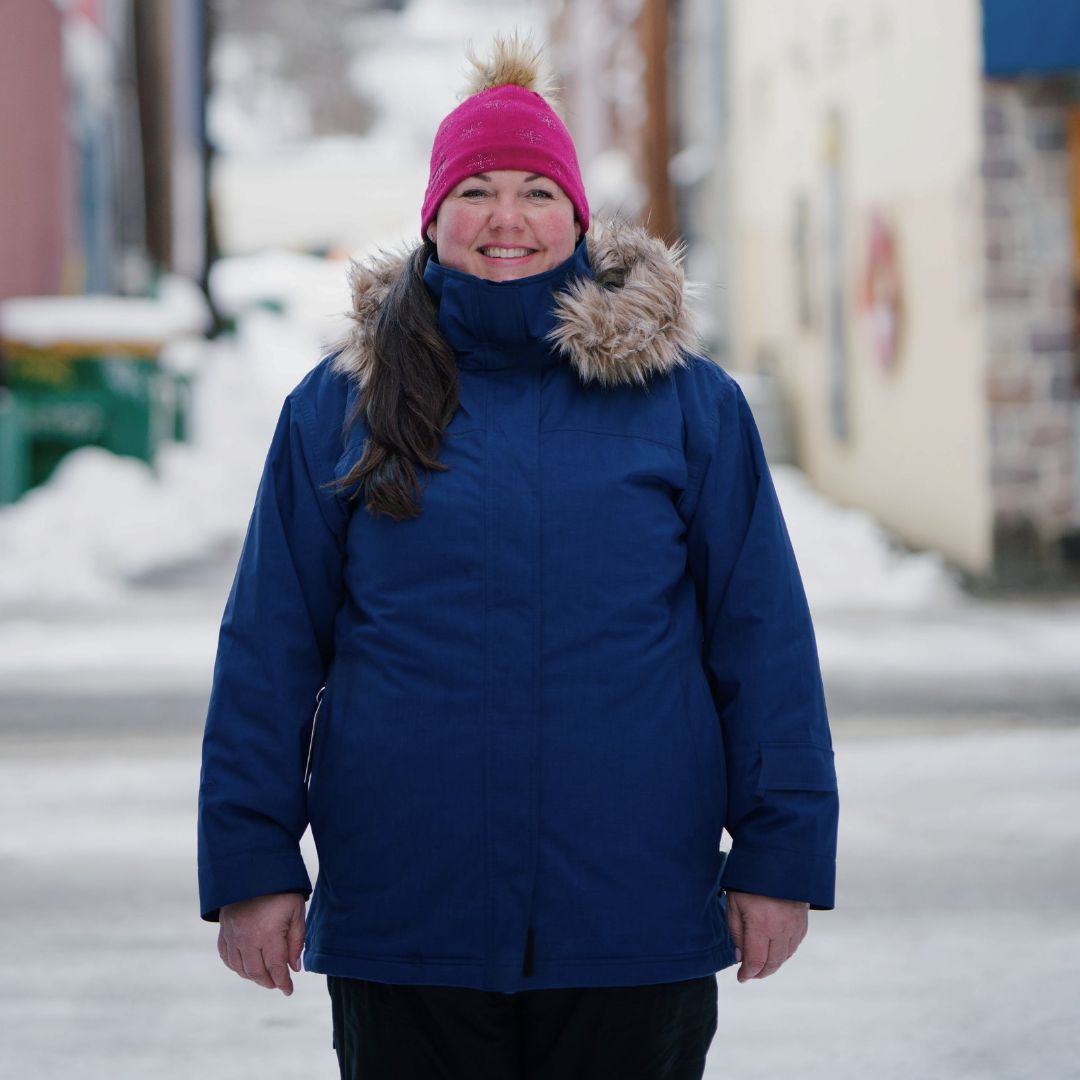 Smiling woman wearing the Cartel Brooklyn Stretch Women's Plus Size Ski Jacket in blue with a faux-fur trimmed hood and a pink beanie.