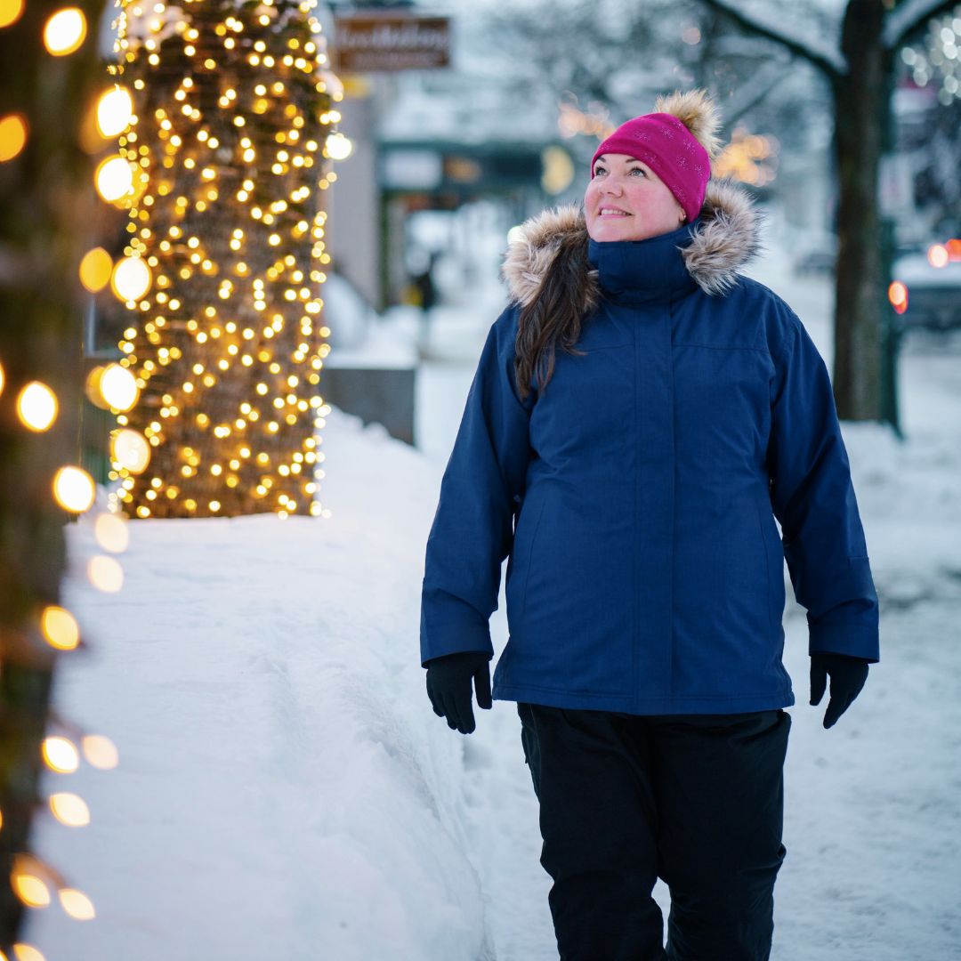 Woman walking down a snowy street at night next to holiday lights, wearing the Cartel Brooklyn Stretch Women's Plus Size Ski Jacket in blue.