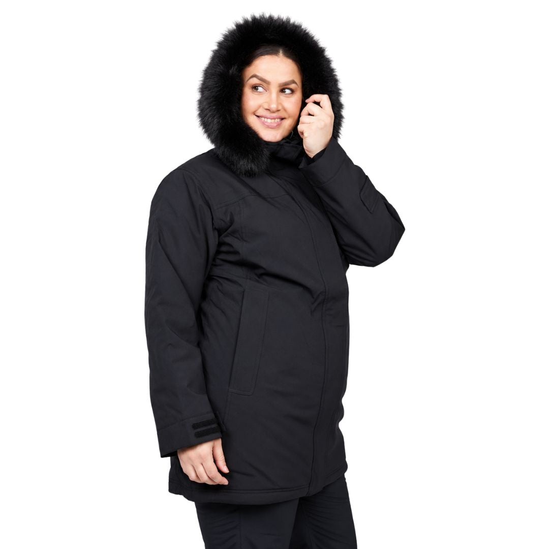 Side view of a smiling woman looking over her shoulder while wearing the plush black faux-fur hood of her black Brooky Long Stretch Jacket.