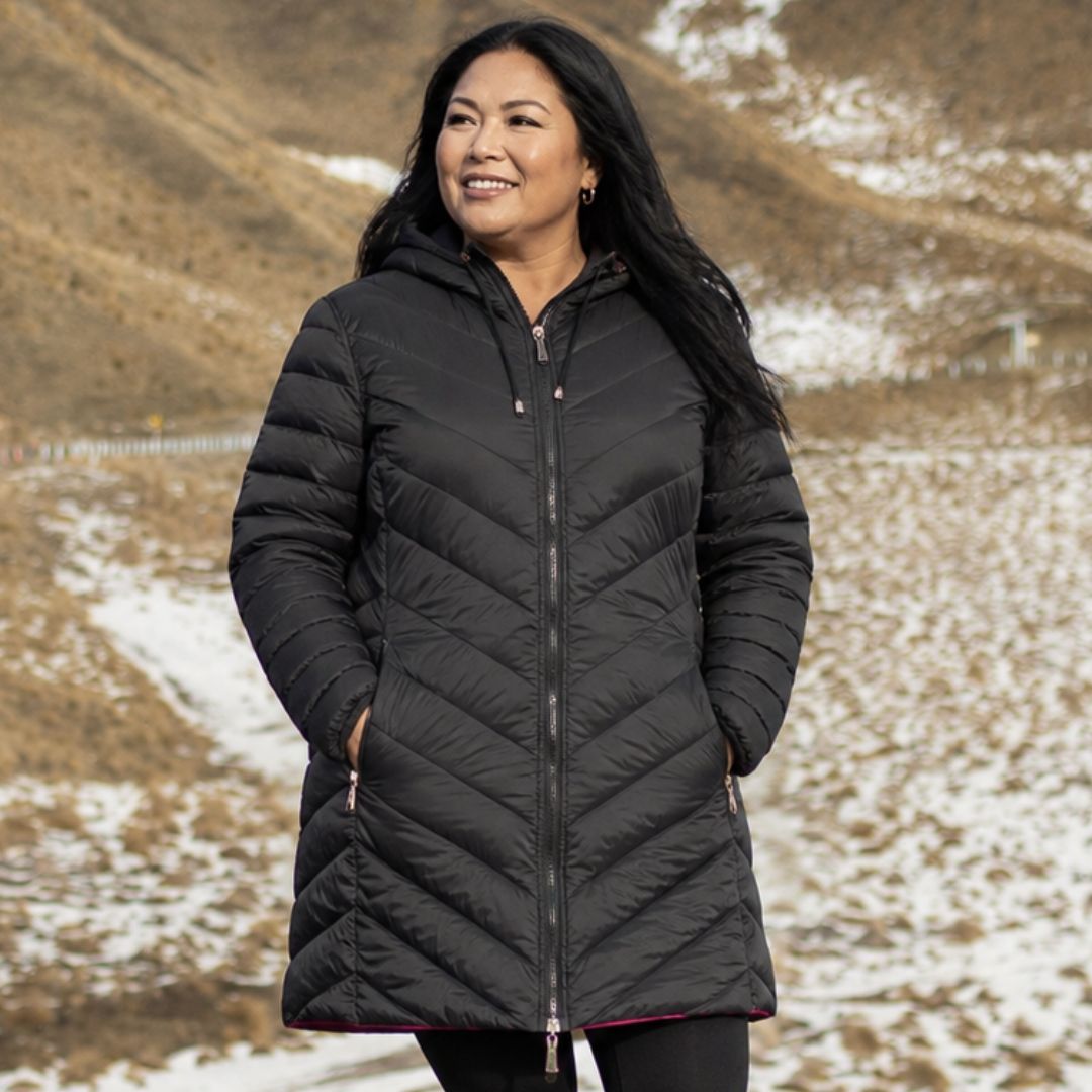 Front view of a smiling woman wearing the fully zipped black side of the reversible Moke Arnie Women's Puffer Coat.