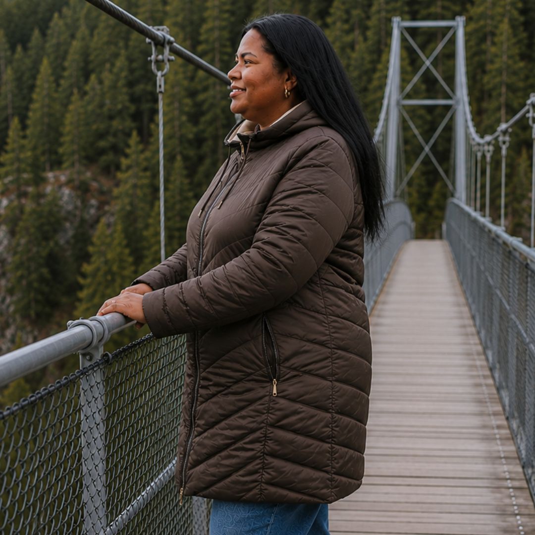 Side view of a woman standing on a suspension bridge wearing the chocolate brown side of the Moke Arnie Women's Reversible Puffer Coat.
