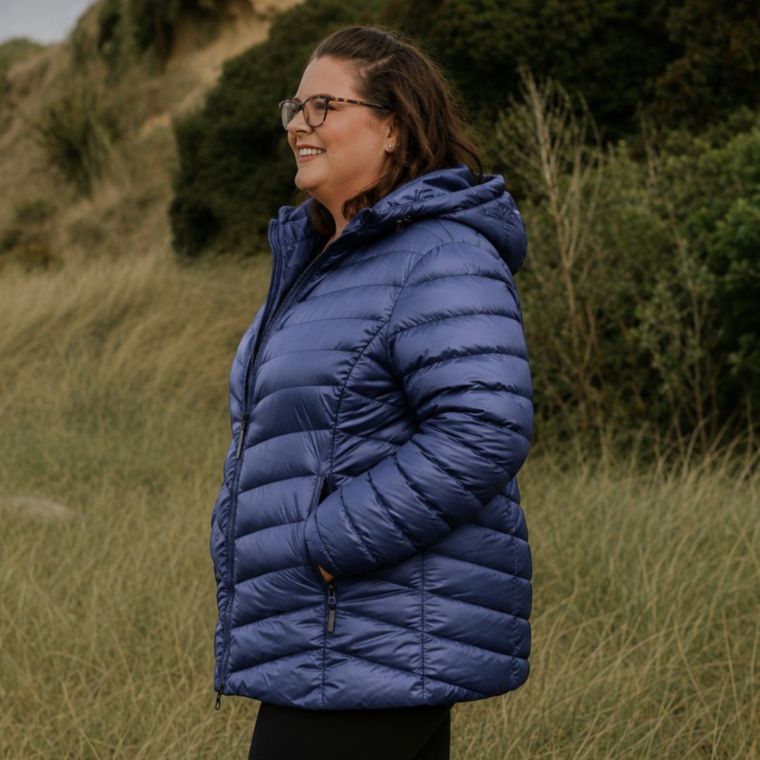 Side profile view of a smiling woman with glasses wearing the Moke Cushla Women's Plus Size Down Jacket in moonlight blue outdoors.