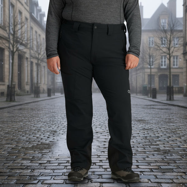 A woman standing, wearing black Outdoor Research Cirque Women's Softshell Pants with a brushed tricot-lined waistband, multiple pockets, and a logo on the left thigh area.