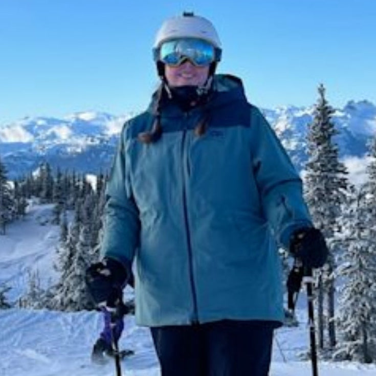 Person skiing on a snowy slope with mountains and trees in the background