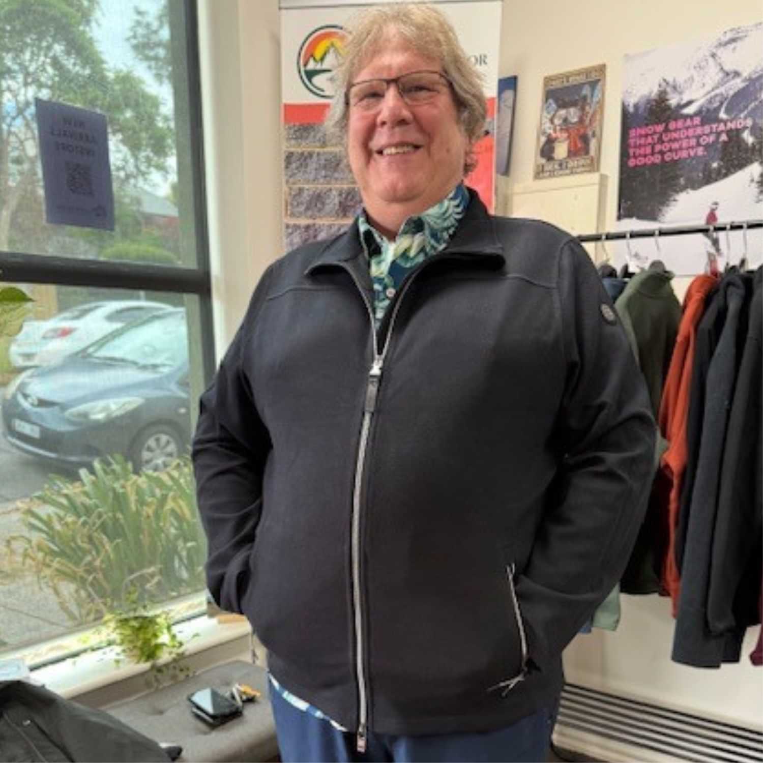 Smiling man with glasses standing indoors with hands in his pockets, wearing a black Stoy Powerstretch Men's Plus Size Zipped Jacket.