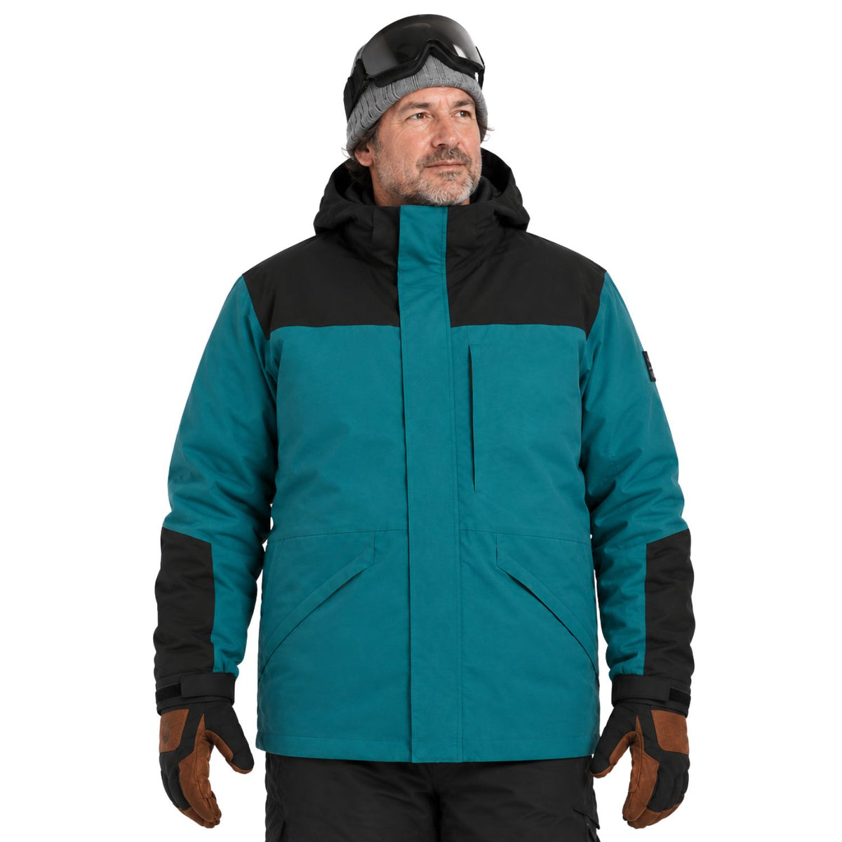 A big man wearing a colorblock ski jacket in teal and black, along with a gray beanie, black goggles, and brown gloves, photographed against a solid white background.