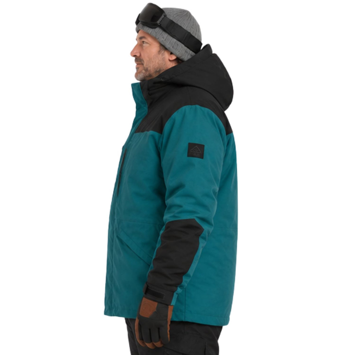 A man in profile wearing a teal and black ski jacket, a gray beanie with goggles, and brown gloves, photographed against a plain white background.