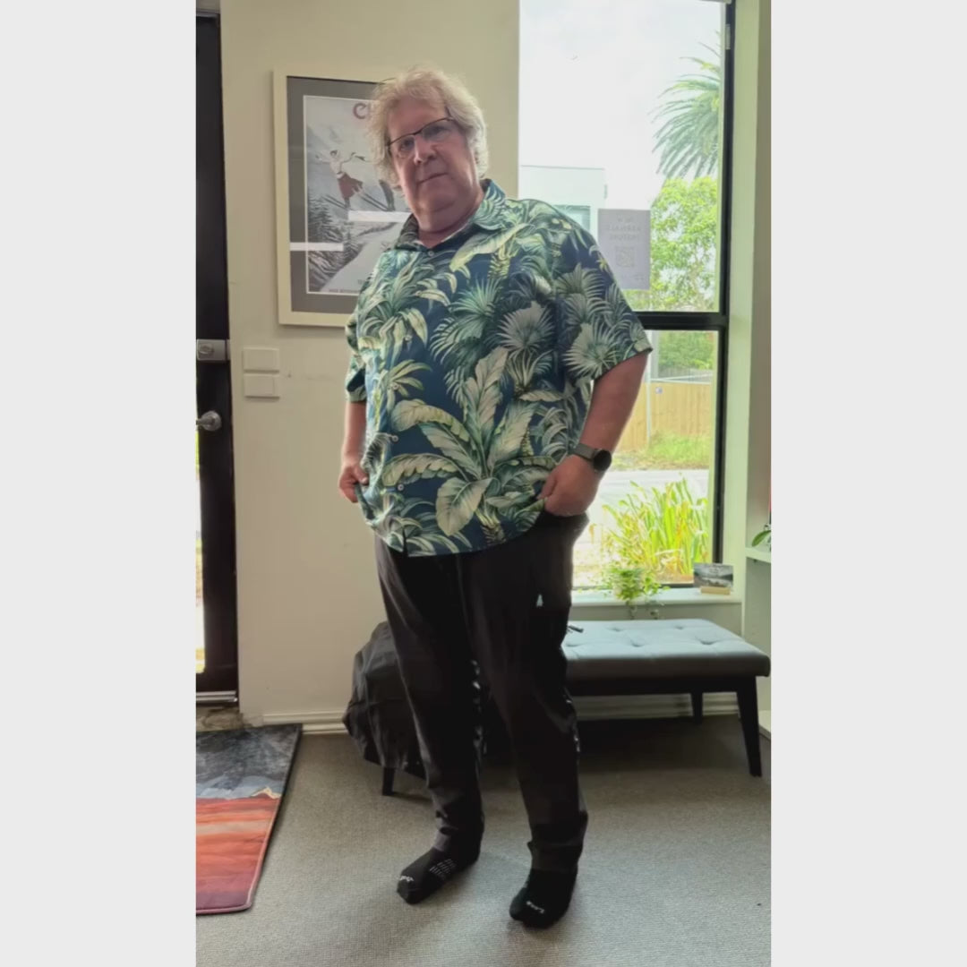 Man wearing Thicket Adventure Brecken Travel Pants BELLY FIT in black, styled with a tropical print shirt indoors, showcasing relaxed comfort and versatile plus size travel fit.